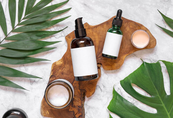Natural cosmetics in glass bottles on a wooden board near tropical leaves, mockup, top view