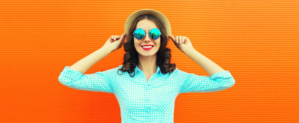 Portrait of young woman wearing summer straw round hat on orange background