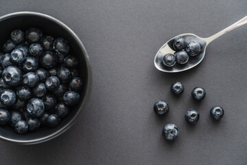 Top view of blueberries in spoon near bowl on black background.