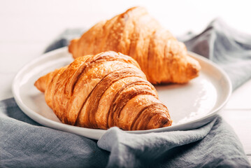 Plate with two fresh croissants on white wooden table.