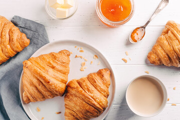Plate with two fresh croissants, jam and coffee on white wooden table. Top view.