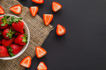 Top view of juicy strawberries in bowl on sackcloth on black background.