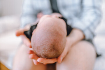 The father holds the newborn on his lap with his head to the camera. Focus on the child's head. The concept of child care and protection