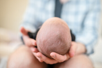 The father holds the newborn on his lap with his head to the camera. Focus on the child's head. The concept of child care and protection