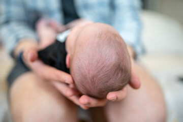 The father holds the newborn on his lap with his head to the camera. Focus on the child's head. The concept of child care and protection