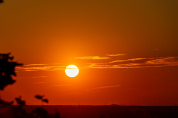 An amazing African sunset over the rolling hills of south Limburg, with the sun as a yellow ball of fire and an orange sky with a few fluffy clouds for some contrast in the sky