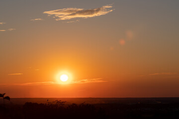 A wonderful sunset with a few fluffy clouds, covering the rolling hills of south Limburg in the Netherlands with an orange and golden glow, creating a magical atmosphere over the agricultural fields.