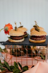 hamburgers with meat cutlet, decorated with cucumber on a skewer, stand on a metal stand on a festive table