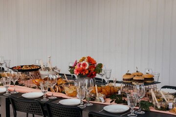 festive snacks are served on a black table decorated with a pink tablecloth and gerberas, against the background of a cozy courtyard