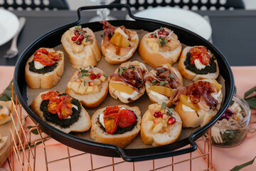 bruschetta with pesto, dried tomatoes, cheese, pomegranate, cheese and pastrami on a black metal tray and a golden lattice stand on the background of a festive table close up