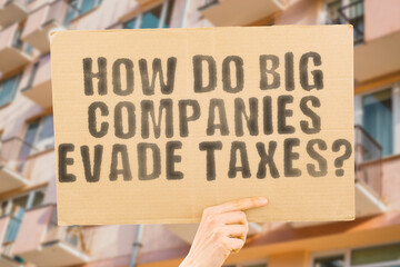The question " How do big companies evade taxes? " is on a banner in men's hands with blurred background. File. Thief. Claim. Contract. Justice. Large. Leak. Bill. Budget. Coin. Control. Cost. Court