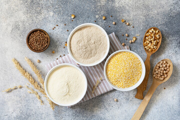 Food and baking gluten free ingredient. Cereals and flours coarse, corn flour, buckwheat flour, chickpeas flour over gray stone background. View from above. - obrazy, fototapety, plakaty