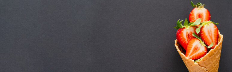 Top view of organic strawberries in waffle cone on black background, banner.