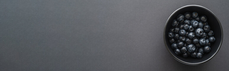 Top view of fresh blueberries in bowl on black surface, banner.