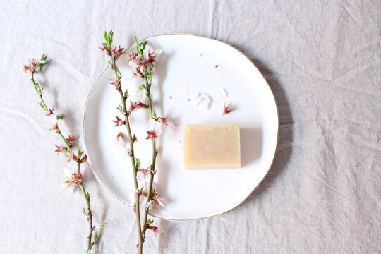 Closeup flowering branch of almond , hand made herbal soap earthenware plate, and white table background. Floral composition, feminine styled stock image. Selective focus. A place for your text.