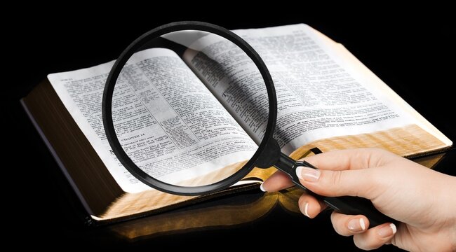 A magnifying glass in hand with open bible book.