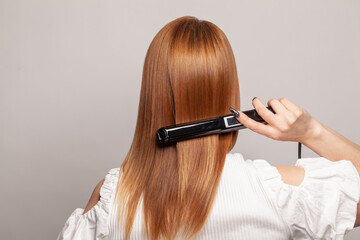Hairdressing. Woman with beautiful long healthy hair using hair straightener