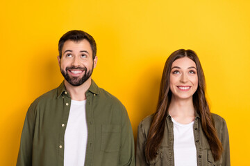 Photo of two cheerful minded people look interested up empty space isolated on yellow color background