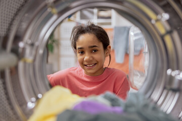 Smiling girl in pigtails unpacks washing machine, takes out colorful wet clean smelling clothes...