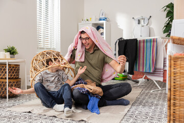 Father and son cleaning in bathroom, laundry room, throwing clothes out of wicker basket, packing things into washing machine, man playing with child, put sheet over head.