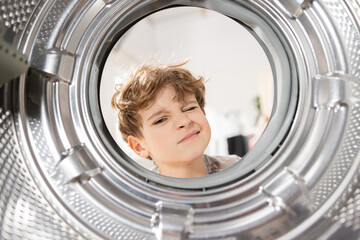 Crooked face strange face of the boy looking with a grimace inside the washing machine, dirty drum...