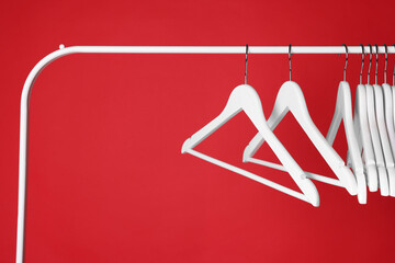 White clothes hangers on metal rack against red background