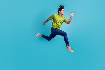 Full length photo of positive excited man wear green t-shirt hurrying jumping high isolated blue color background