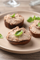 Slices of bread with delicious pate and basil on wooden table, closeup