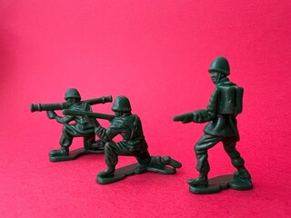 敵へ向けて銃を構える3人の兵士の人形（赤背景）、戦争イメージ