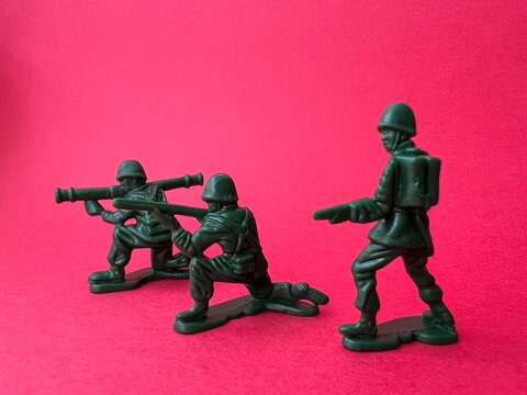 敵へ向けて銃を構える3人の兵士の人形（赤背景）、戦争イメージ