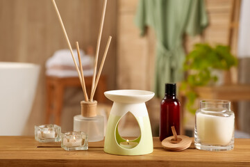 Aroma lamp, bottle of oil, candles and air reed freshener on wooden table in bathroom