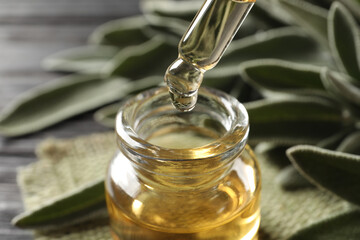 Dropping essential sage oil into bottle on blurred background, closeup
