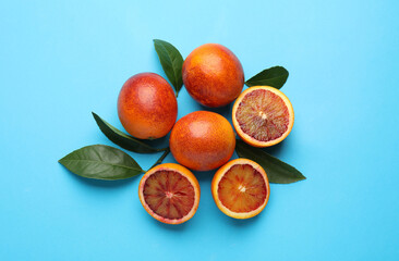 Many ripe sicilian oranges and leaves on light blue background, flat lay