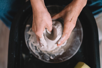 Female sculptor making clay pot on pottery wheel