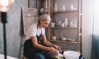 Female sculptor making clay pot on pottery wheel - obrazy, fototapety, plakaty