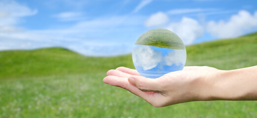 Crystal sphere in hand with green hill and blue sky background. World environment day, global...
