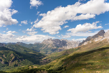 general view of a valley with the Picos de Europa and the cloudy blue sky in the background