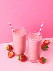 Two glasses of strawberry smoothie or milkshake on pink background