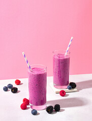 Two glasses of purple wild berry smoothie or milkshake on pink background