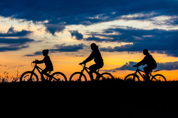 Plakat family cyclist and bicycle silhouettes on the dark background of sunsets. mom and her children ride bicycles against the backdrop of sunset.