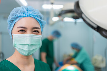 Fototapeta na wymiar Portrait of Asian woman surgeon with medical mask standing in operation theater at a hospital. Team of Professional surgeons. Healthcare, emergency medical service concept