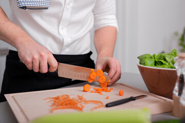 Man preparing vegetarian food meal cutting carrot on cutting board. Homemade meal