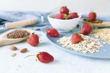 Fresh strawberries on a plate, nuts and seeds, on a background of gray linen fabric, healthy breakfast ingredients