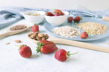 Fresh strawberries on a plate, nuts and seeds, on a background of gray linen fabric, healthy breakfast ingredients