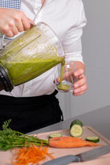 Unrecognizable man making green homemade smoothie in blender and pouring to glass. Healthy lifestyle concept.