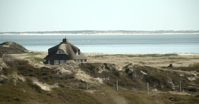 Tiny house with thatched roof on Sylt in a dune landscape with the Northsea and the coastline in the background 4k 60fps