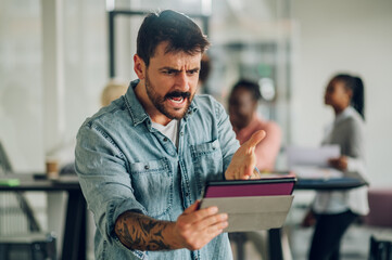 Angry business man using tablet in the office with his team working in the back