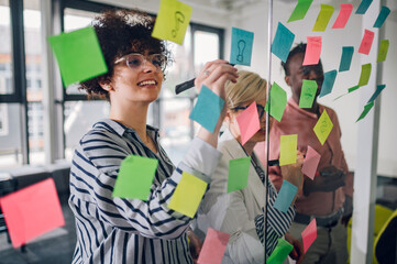 Multiracial team at work writing ideas on sticky notes on the glass wall