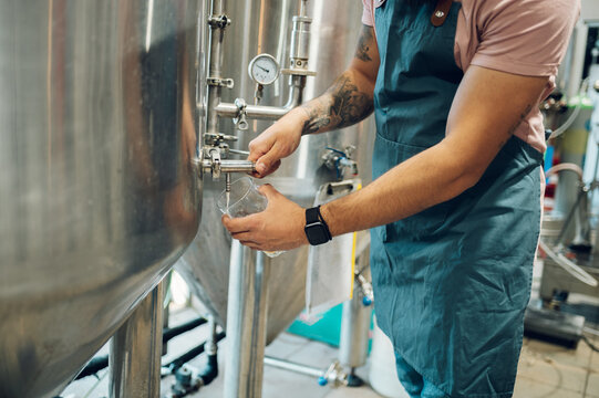 Close shot of a man filling glass of beer on a tap in brewery