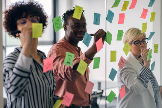 Multiracial team at work writing ideas on sticky notes on the glass wall